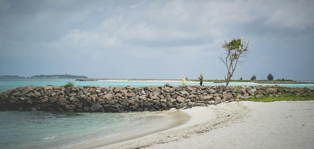 Ava exploring a peaceful Maldives beach with clear water and stone breakwater