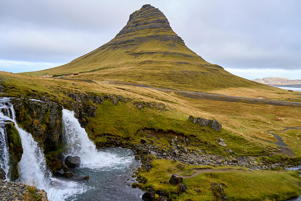 Iconic Kirkjufell peak with flowing waterfall and green hills in Iceland