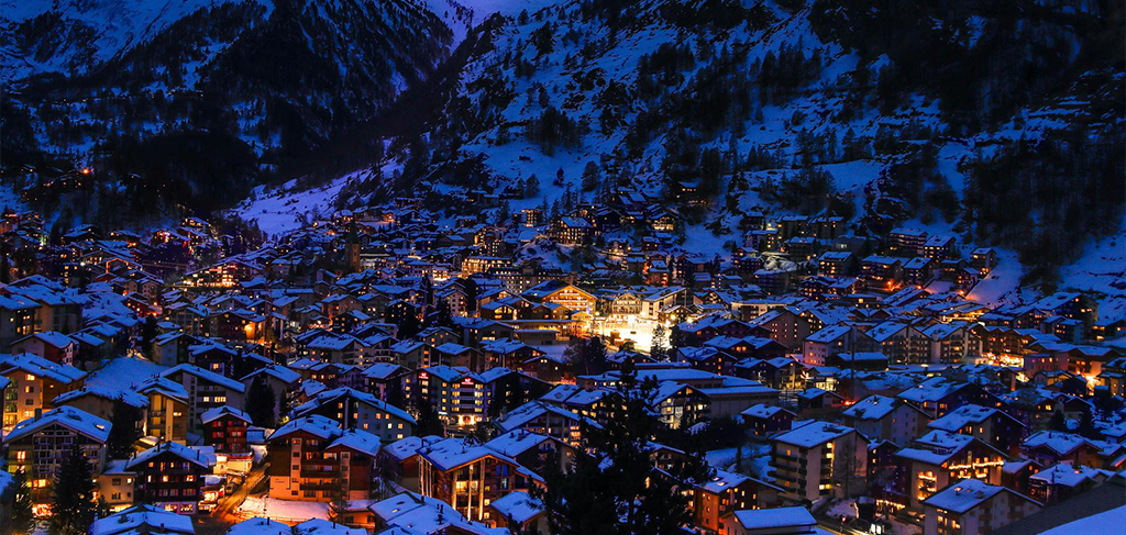 Night view of Zermatt covered in snow with glowing chalet lights and surrounding alpine mountains